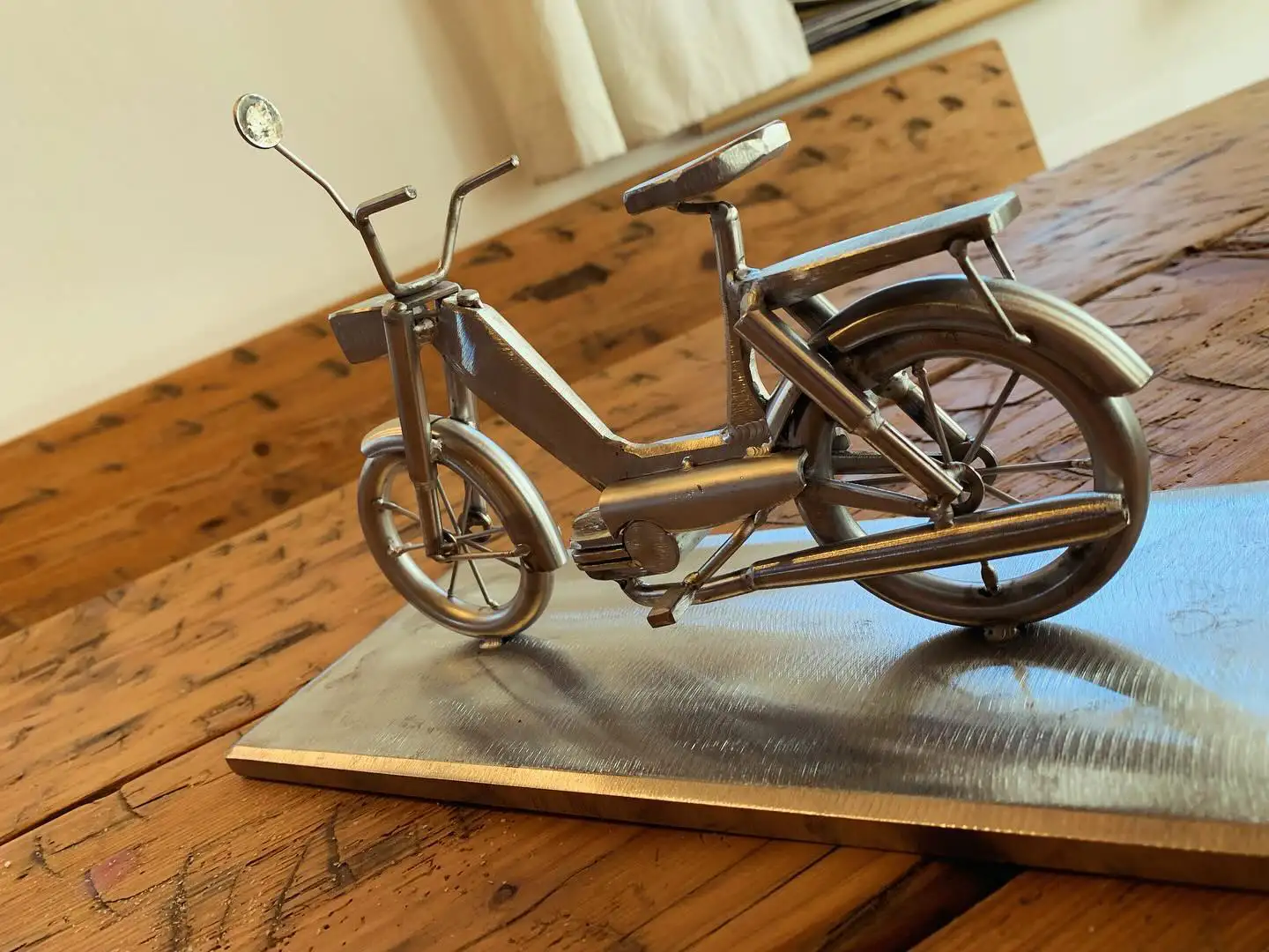 Metallskulptur eines Mopeds von der Seite auf Holztisch