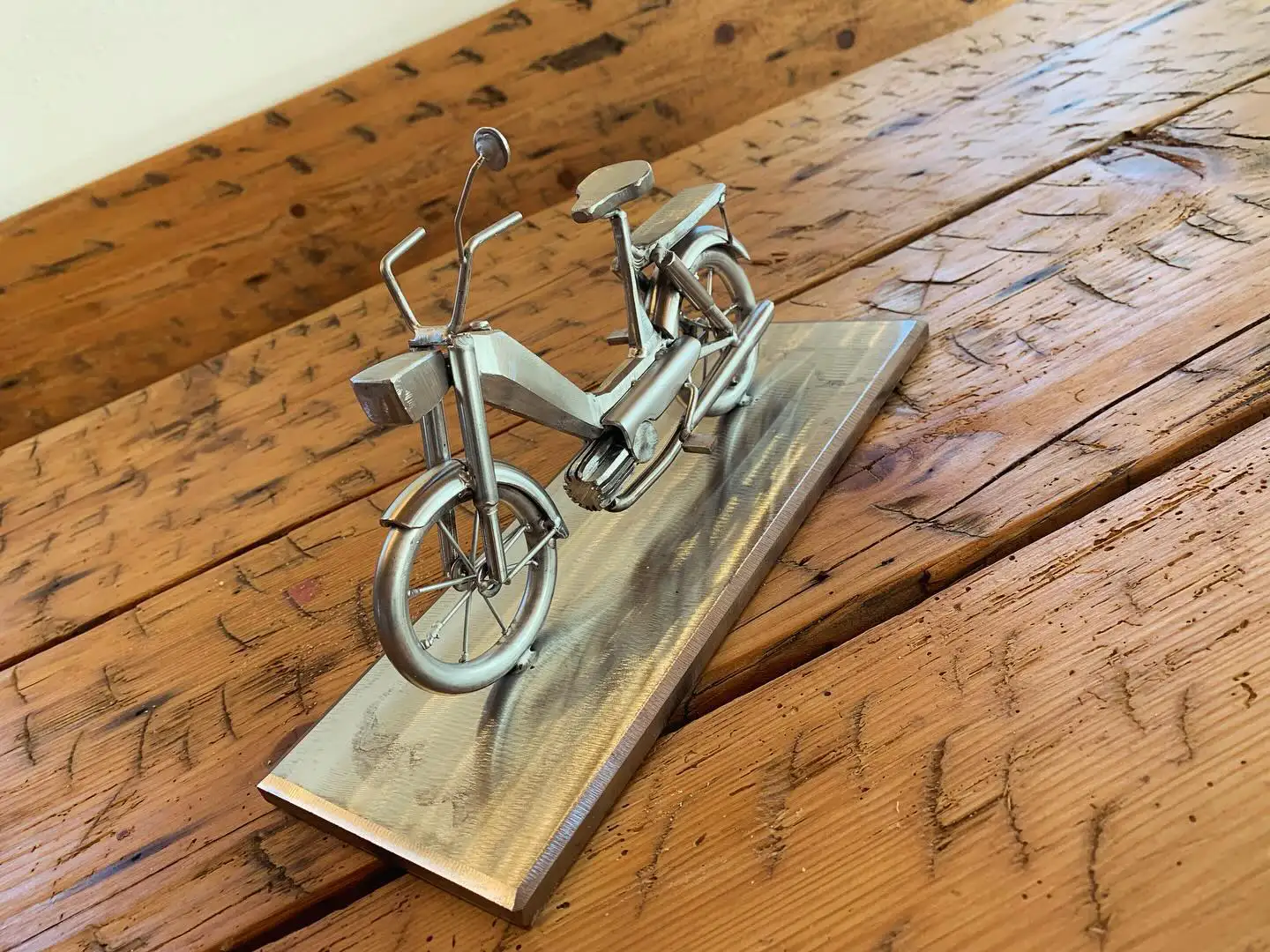 Metallskulptur eines Mopeds auf einer Stahlplatte auf Holztisch