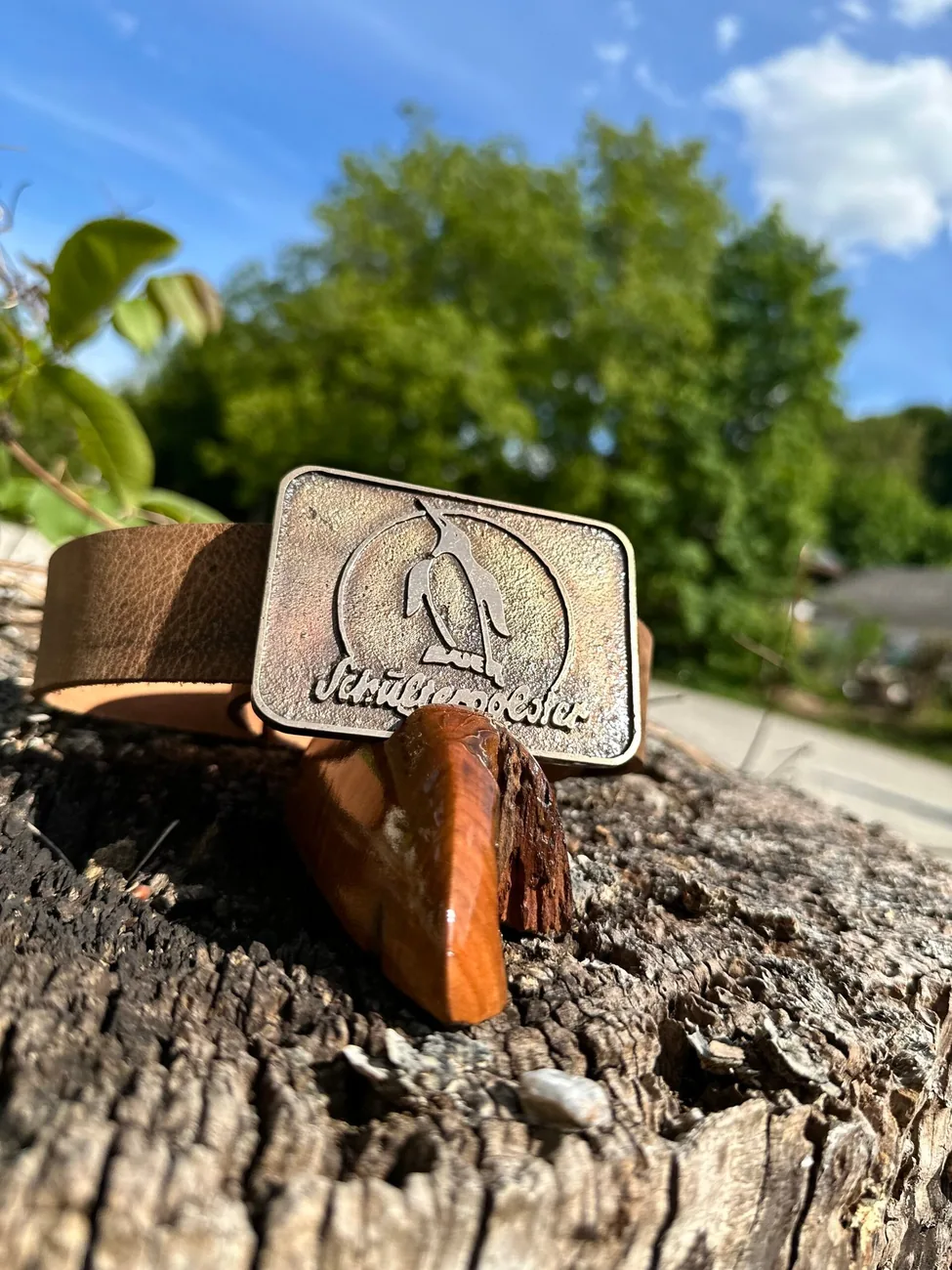 Gürtelschnalle mit Brauerei-Logo auf einem Baumstumpf